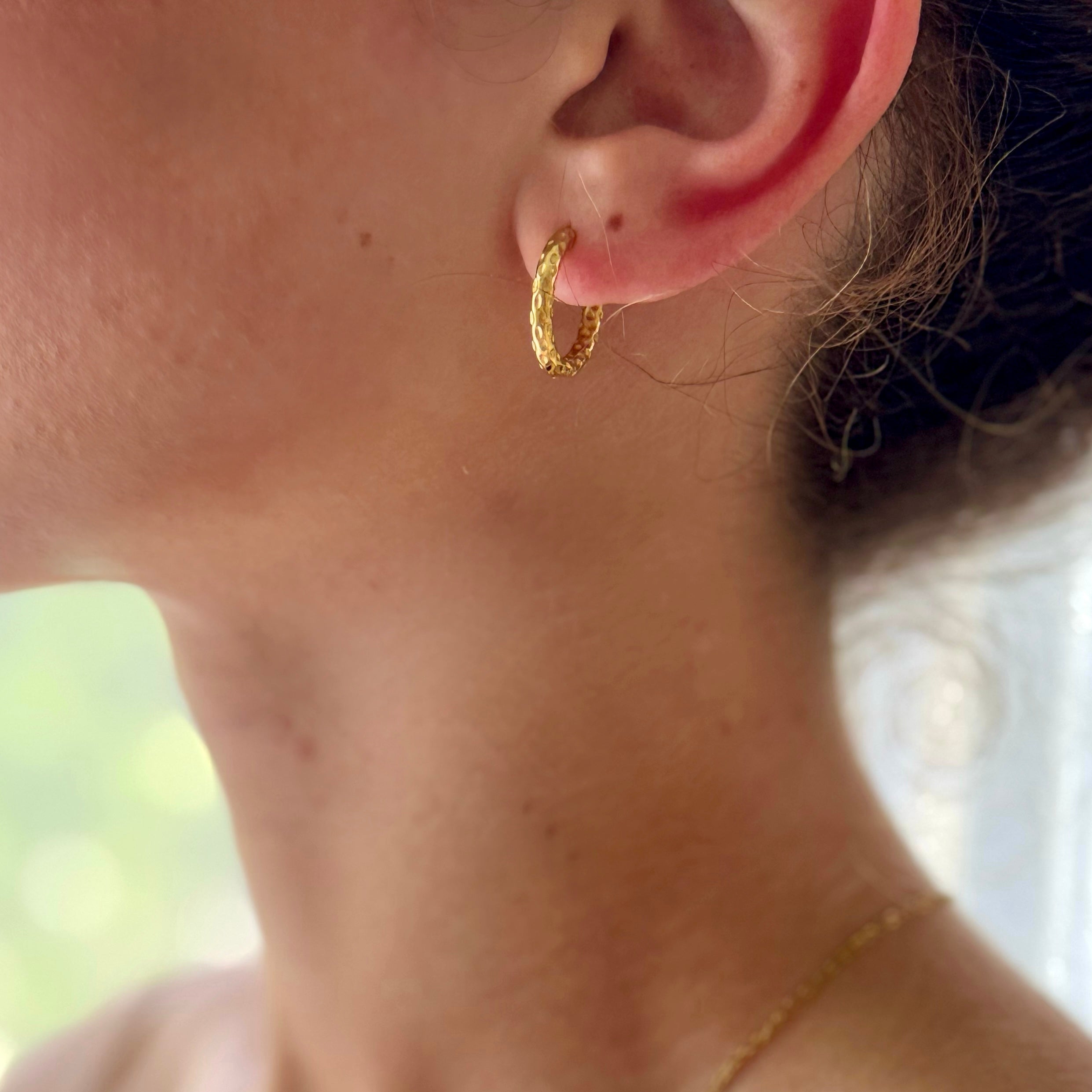 Close-up of a person wearing gold hoop earrings and a necklace.